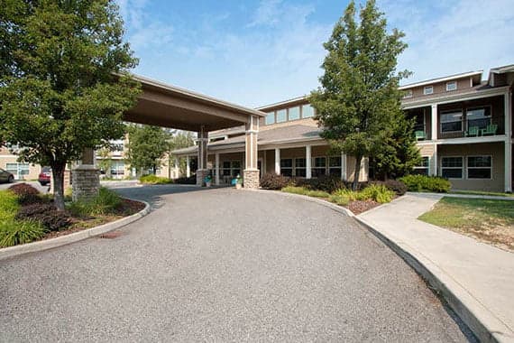 An inviting building entrance with a covered driveway and landscaped surroundings under a clear sky.
