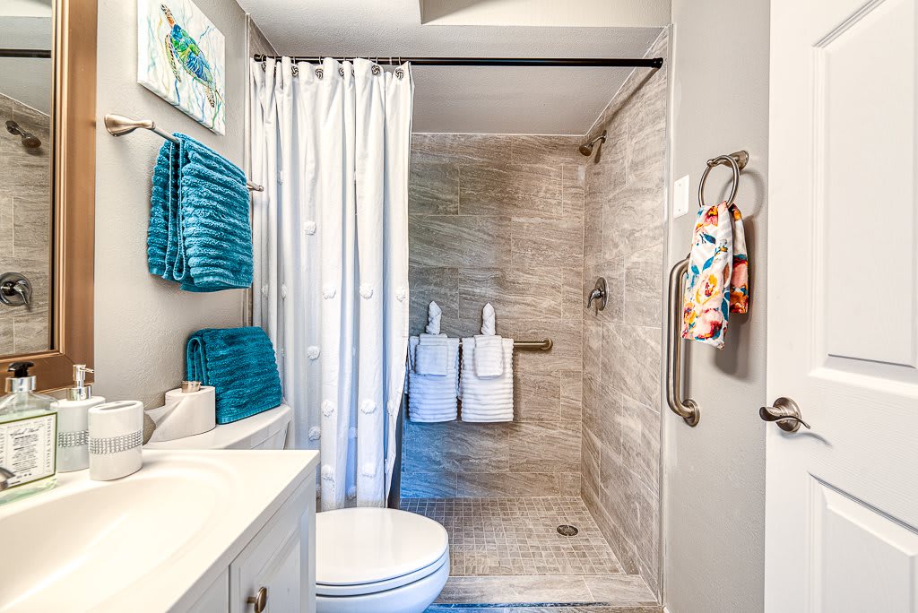 A modern bathroom with a shower area, featuring turquoise towels and a white shower curtain.