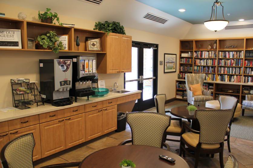 A cozy cafe area featuring a coffee station, tables, chairs, and a bookshelf.