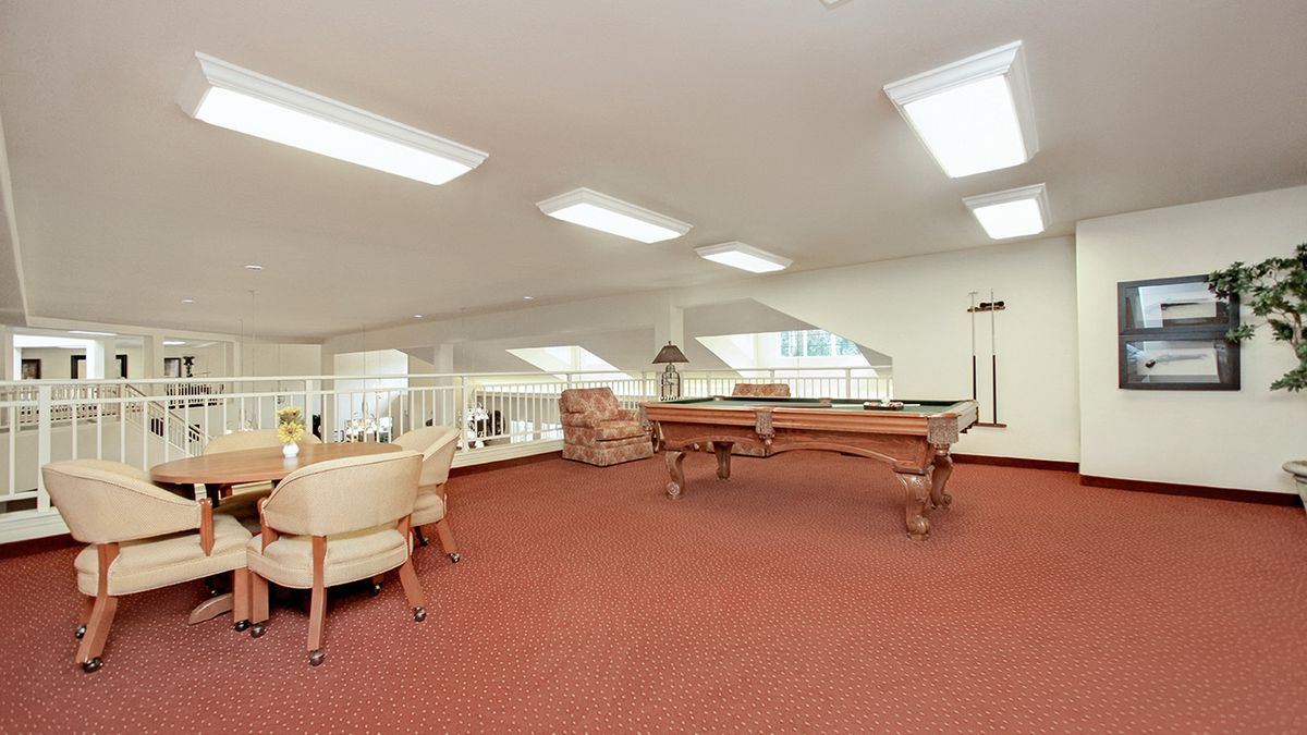 A spacious game room with a pool table and comfortable seating under bright ceiling lights.