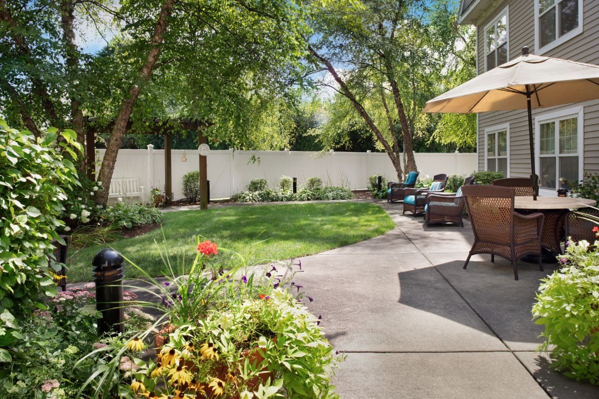 A charming backyard with a patio, garden, and outdoor seating under a sunny sky.