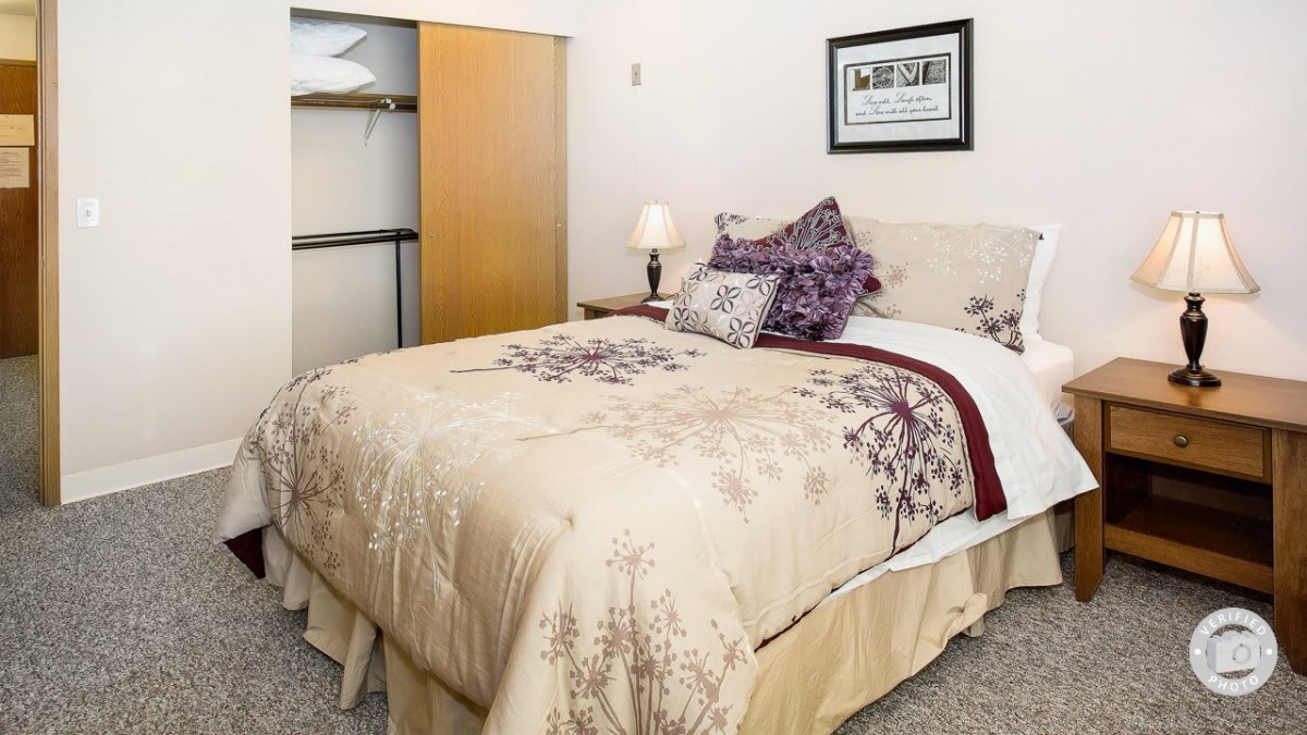 A cozy bedroom with a neatly made bed, decorative pillows, and an open closet.
