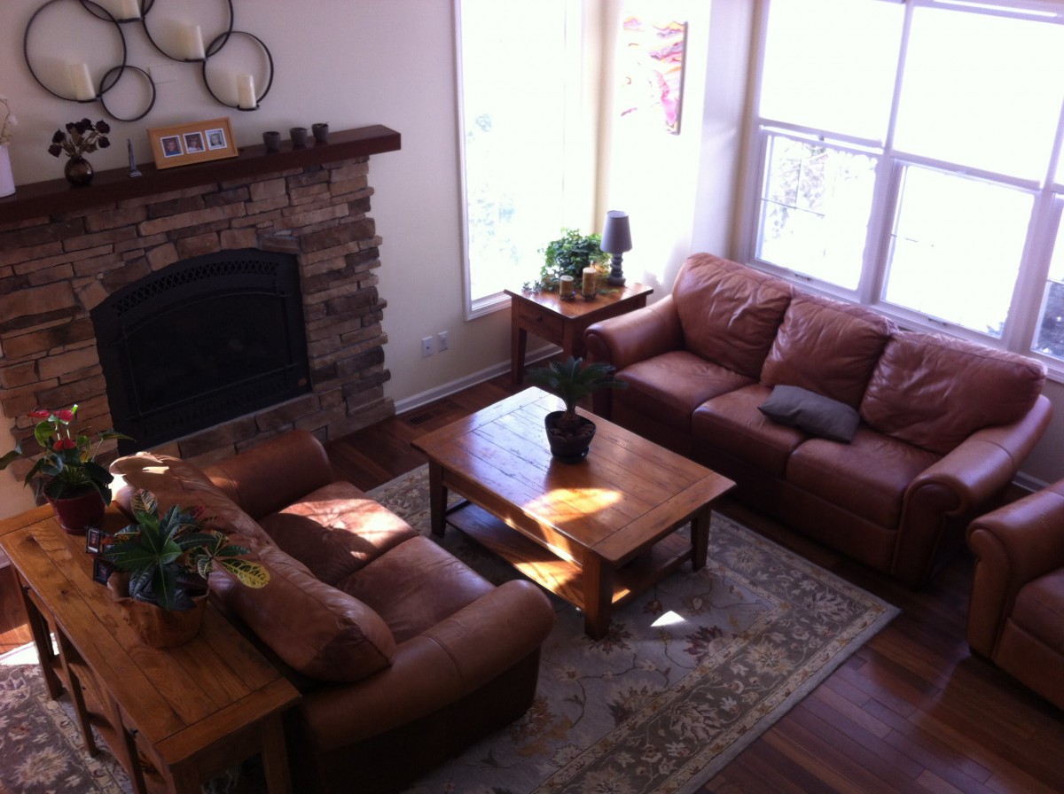 A cozy living room featuring leather sofas, a wooden coffee table, and a fireplace, bathed in natural light.
