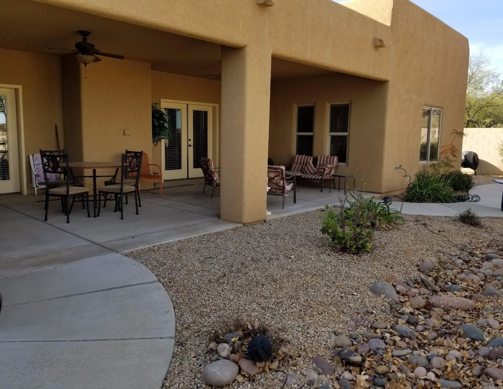 A cozy patio with outdoor seating and desert landscaping, featuring a covered area for shade.