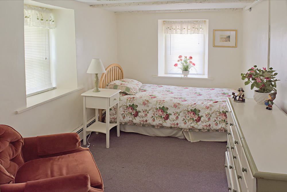 A cozy bedroom with a floral-patterned bedspread and a soft armchair.