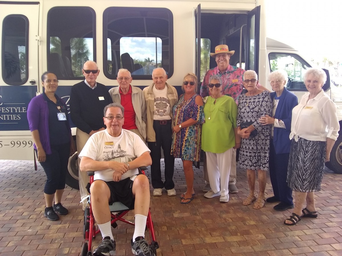 A group of seniors poses in front of a minibus, with one person seated in a wheelchair.