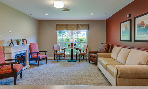 A cozy living room with a sofa, chairs, and a table near a bright window.