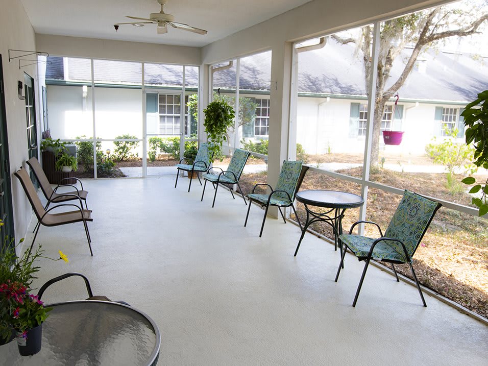 A screened porch featuring several chairs and tables, providing a relaxing outdoor seating area.