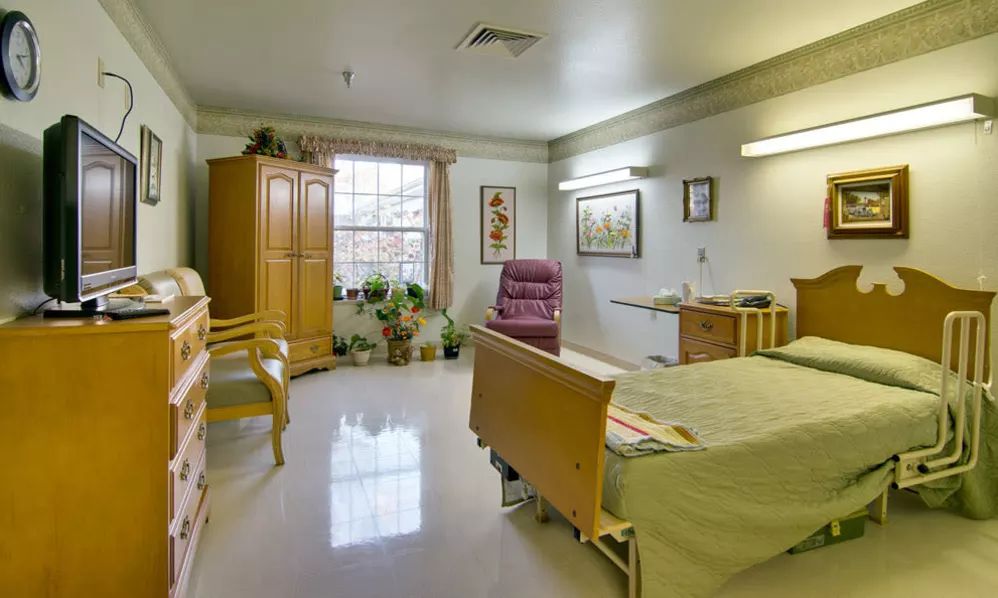 A well-furnished hospital room featuring a bed, a wheelchair, and decorative elements.