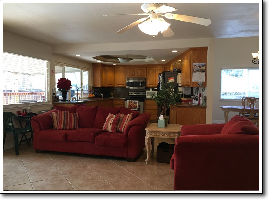 A cozy living room with red sofas, an adjacent kitchen with wooden cabinets, and a ceiling fan overhead.