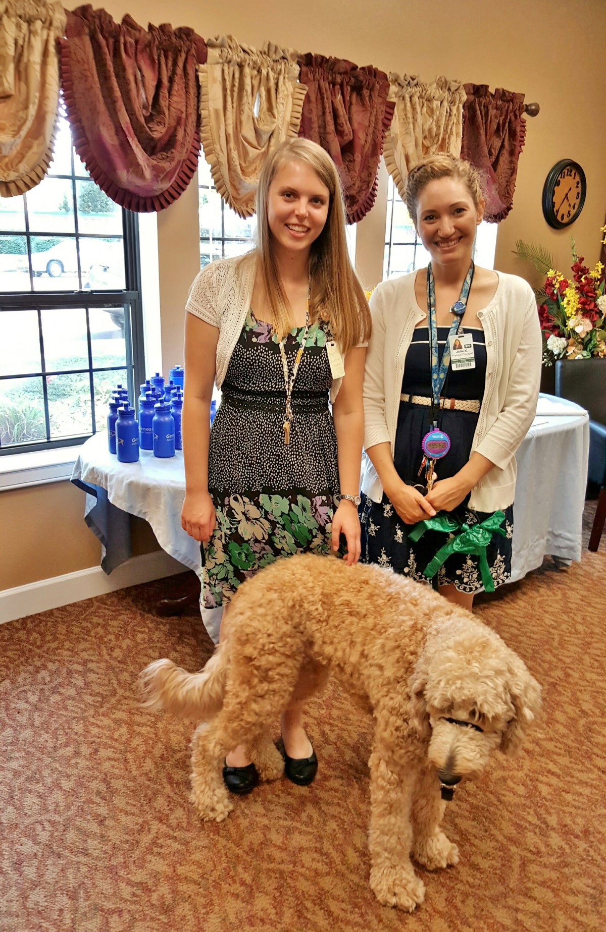 Two women posing indoors with a dog at an event.