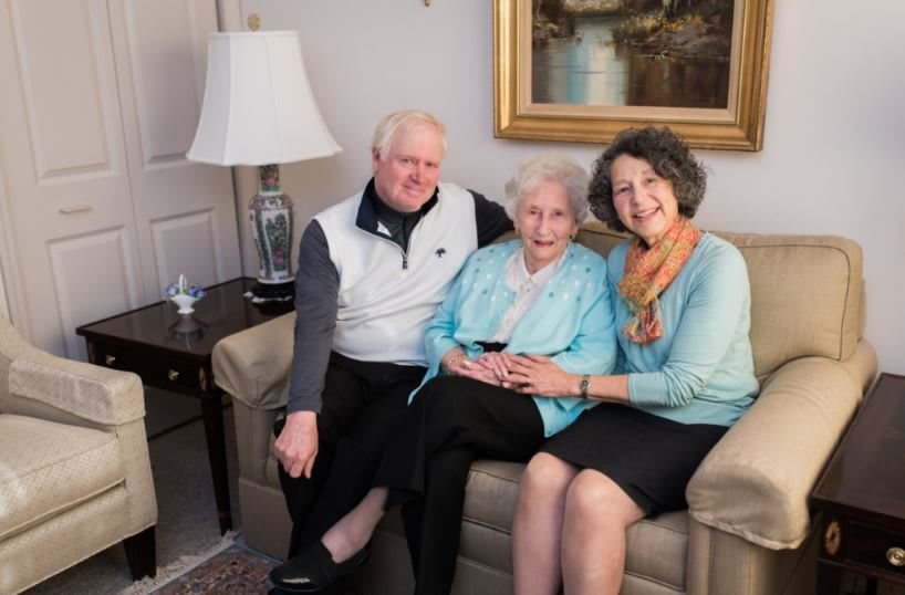 A family sitting together on a sofa, smiling warmly in a cozy room.