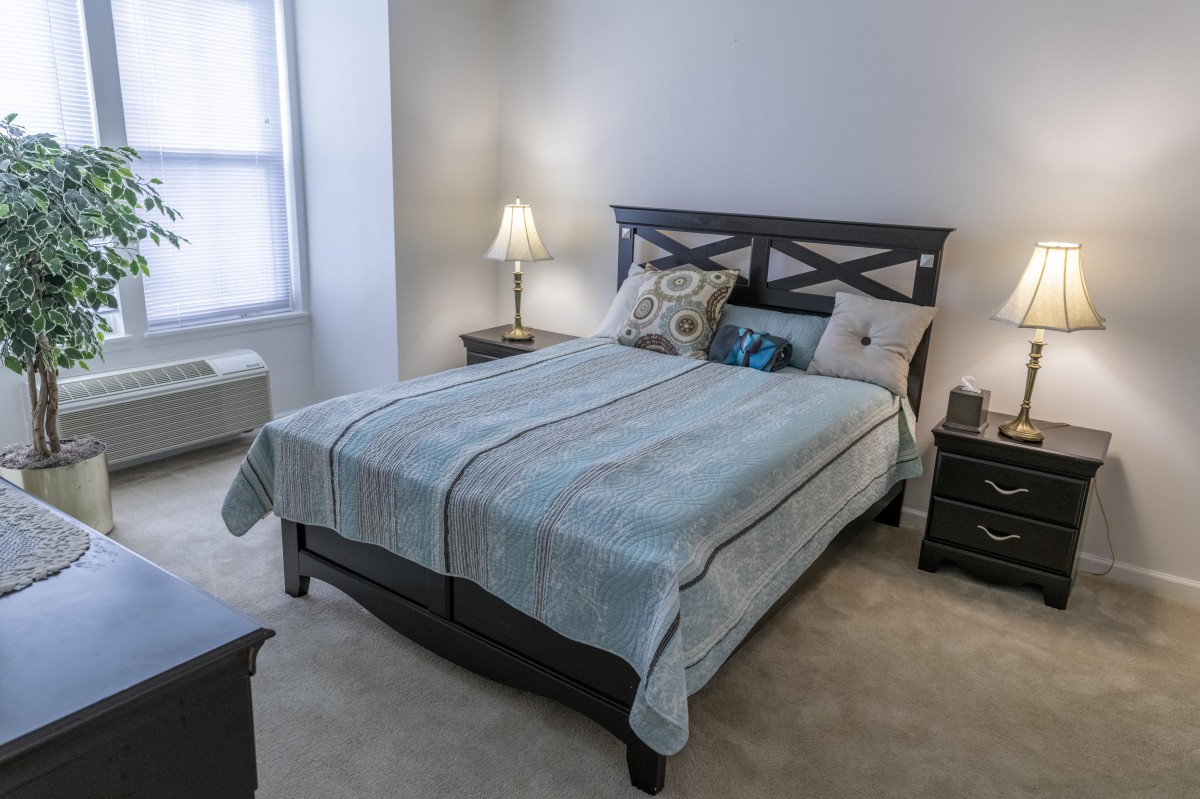 A cozy bedroom with a neatly made bed, flanked by nightstands and illuminated by a soft lamp.