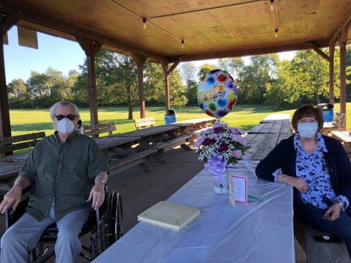 A small outdoor gathering with masked individuals enjoying a celebration under a picnic pavilion.