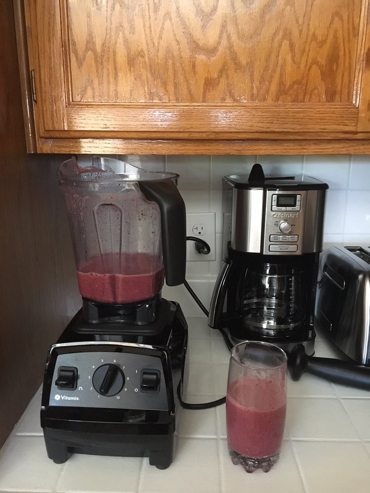 A kitchen countertop with a blender making a smoothie next to a coffee maker.