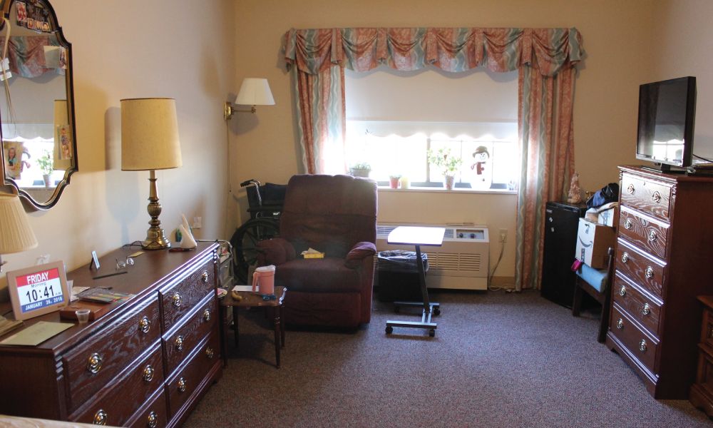 A cozy living room with an armchair, dresser, and window with curtains.