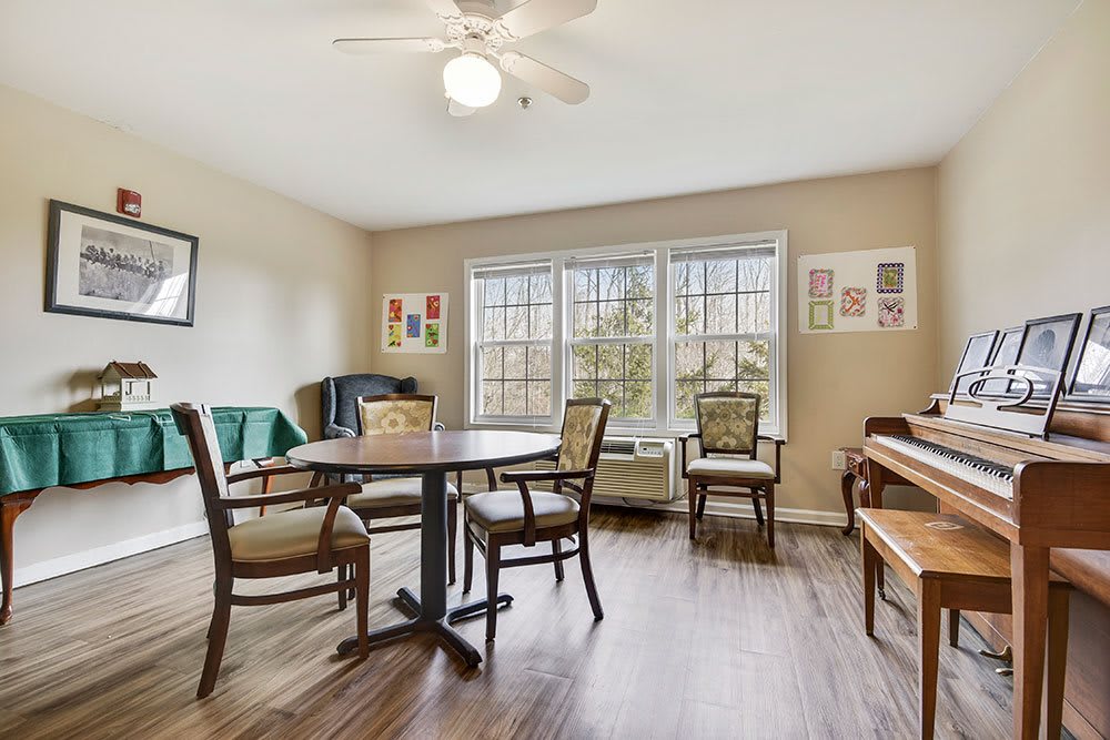 A cozy living room with a dining table set, piano, and large windows.