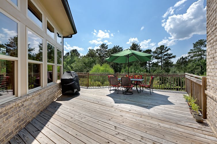 A sunny outdoor deck with a dining set and umbrella, surrounded by nature.