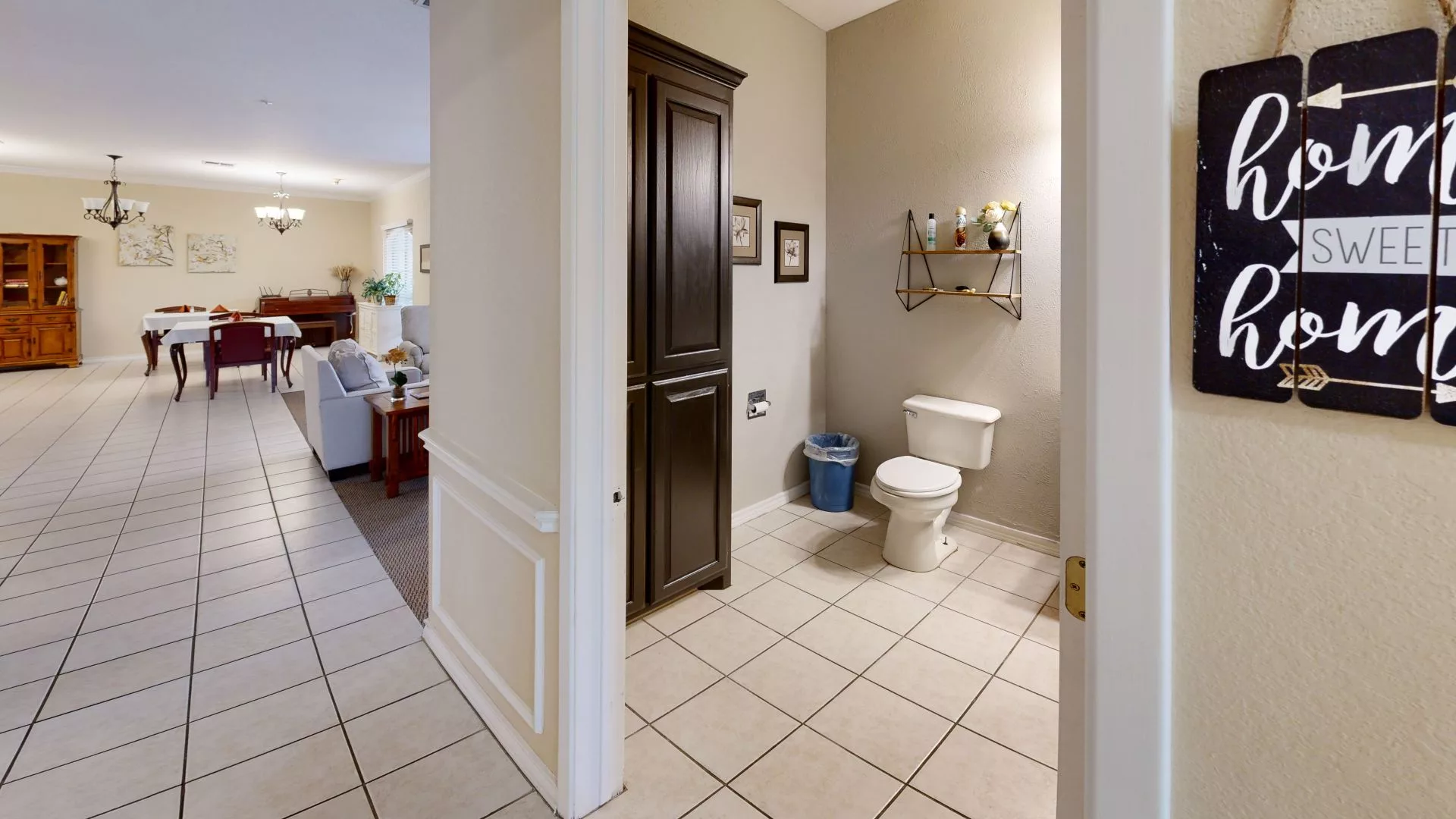 A view of a bathroom with a toilet, tile flooring, and a dark wooden cabinet.