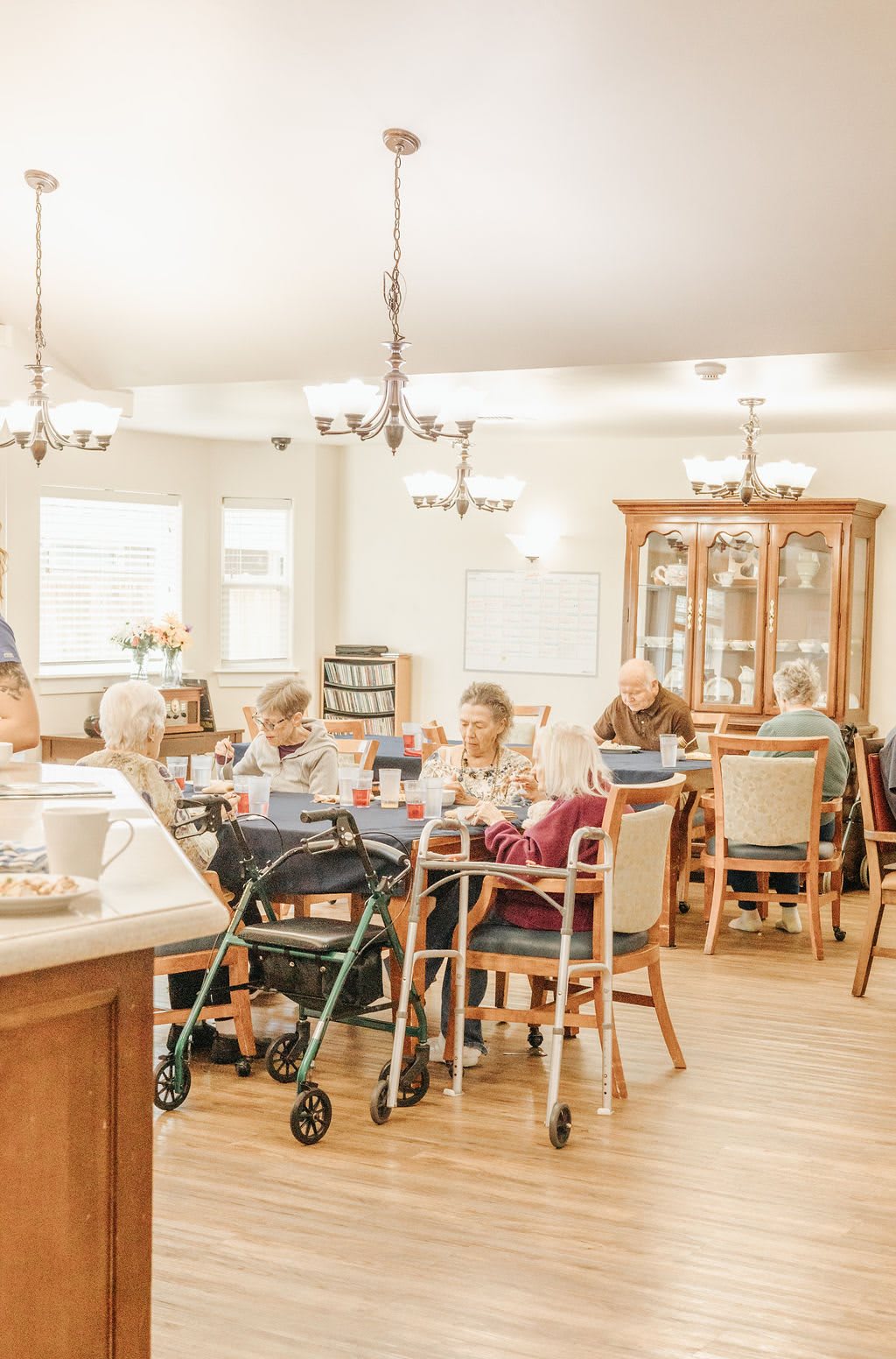 A group of elderly individuals in a nursing home dining area, engaging in conversation.