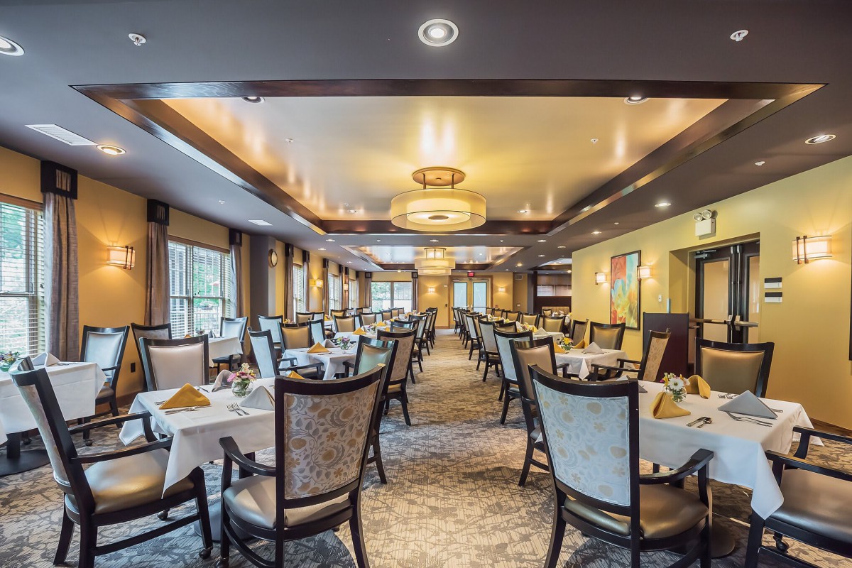 An elegantly decorated restaurant dining room with neatly arranged tables and chairs illuminated by stylish overhead lighting.