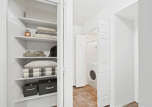 A spacious and organized laundry room featuring white cabinetry, neatly arranged shelves, and a washer/dryer unit.