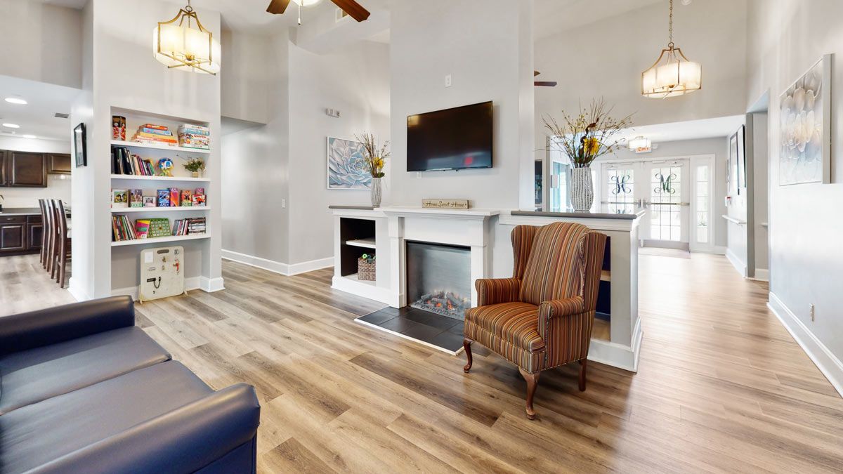 A modern living room with hardwood flooring, featuring a fireplace, mounted television, and a cozy armchair.