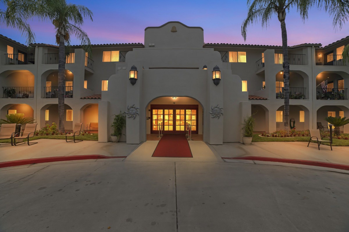 A beautifully illuminated hotel entrance at dusk with palm trees lining the driveway.