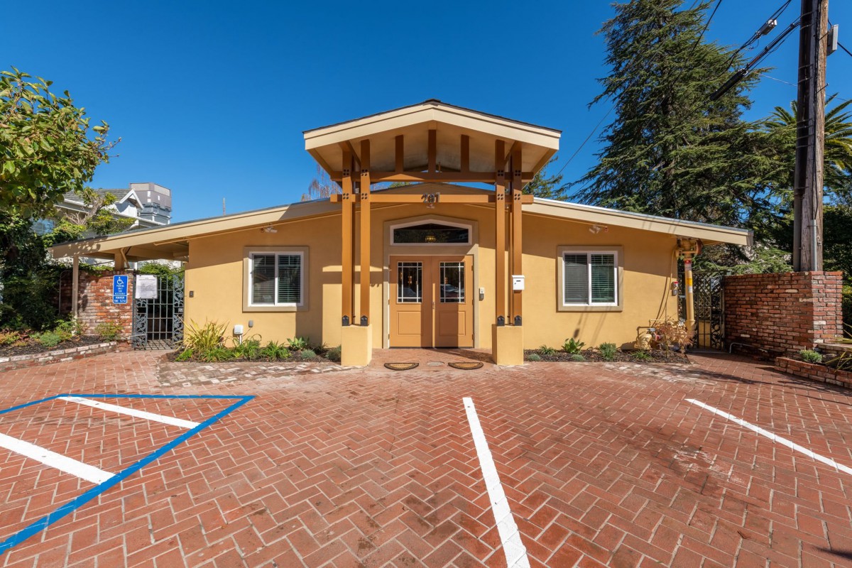 A yellow building with a pitched roof and parking spaces in front, set against a clear blue sky.