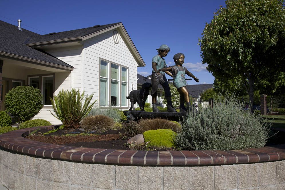 A sculpture of two children and a dog in a landscaped garden outside a house.