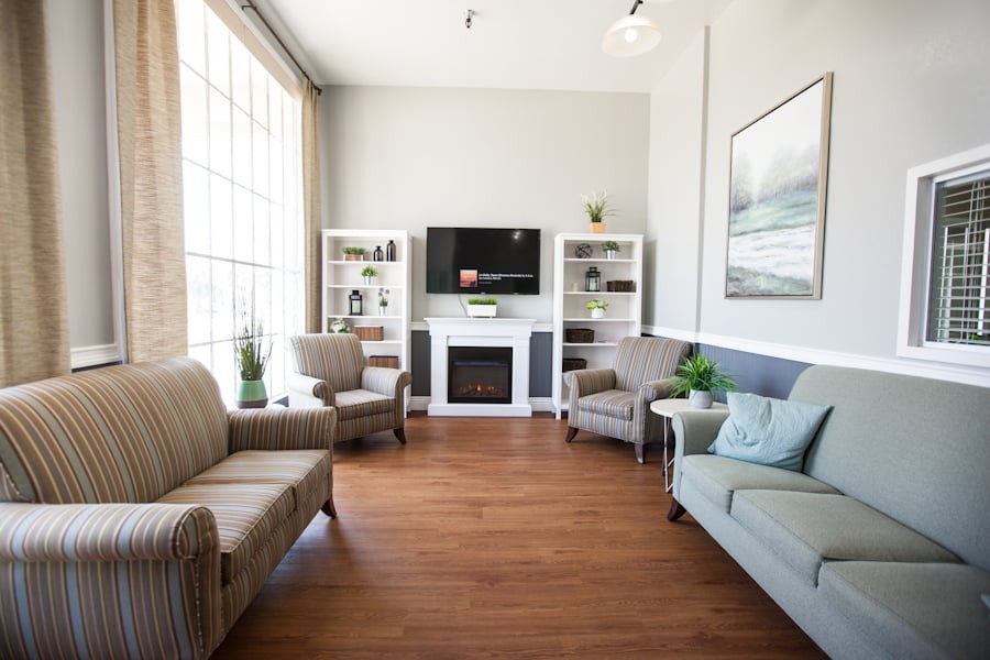 A cozy living room featuring comfortable seating, a television above a fireplace, and bookshelves with decorative items.