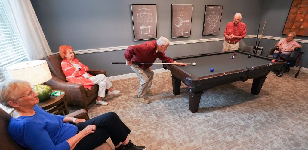 Seniors enjoy a game of billiards together in a cozy room.