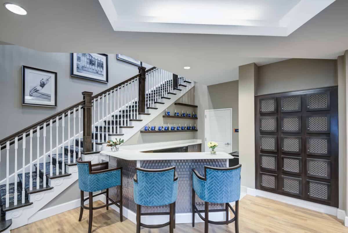 A modern home bar with blue chairs and a stylish staircase.
