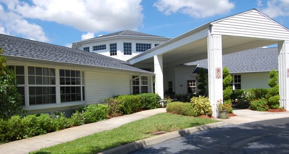A well-maintained building with a covered entrance, surrounded by lush greenery under a partly cloudy sky.