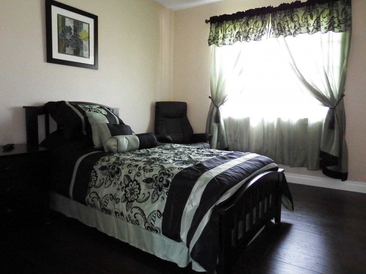 A well-lit bedroom with a single bed and stylish decor, featuring a window with curtains and a cozy chair.