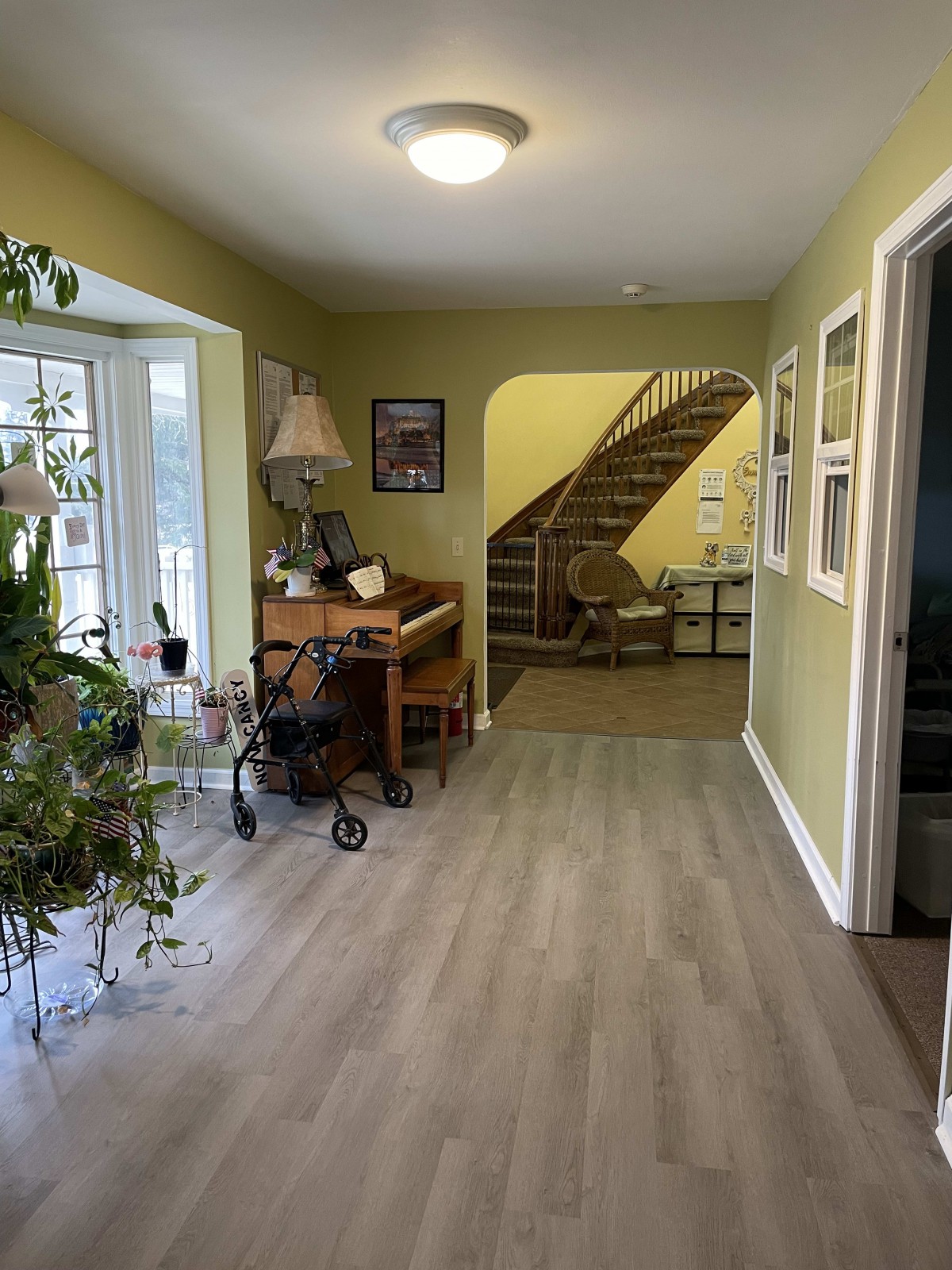 A cozy living area with a piano, plants, and a staircase leading to another floor.