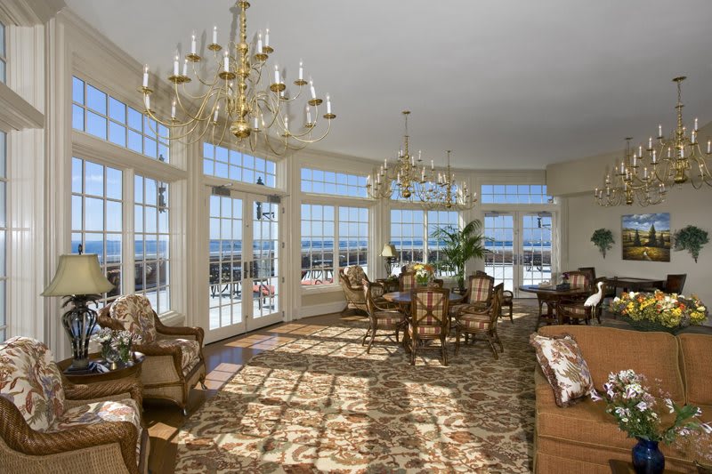 A luxurious living room with large windows and elegant chandeliers, filled with natural light.