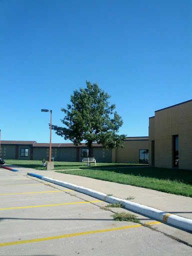 A view of a school building under a clear blue sky, featuring a tree and grassy area.