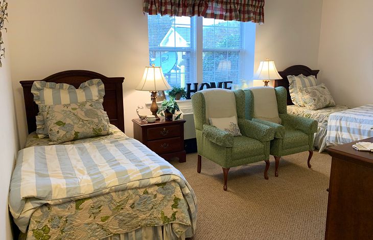 A cozy bedroom with two beds, green armchairs, and warm lighting.