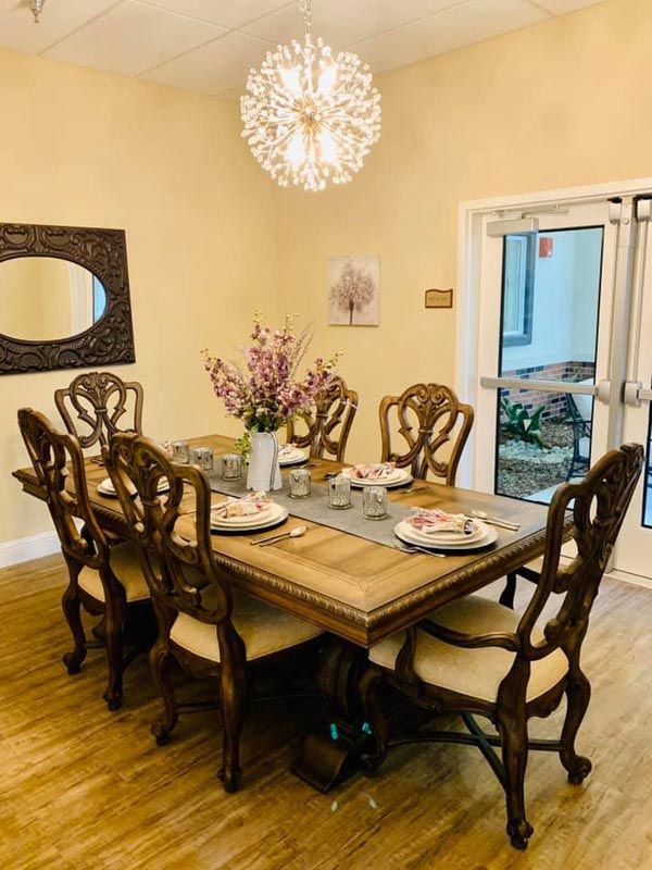 An elegantly set dining room with a wooden table, matching chairs, and a decorative chandelier overhead.