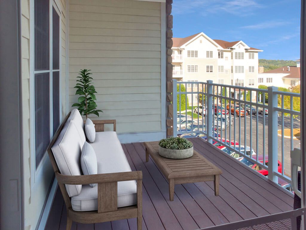 A cozy balcony with cushioned seating and a small table overlooking an apartment complex.