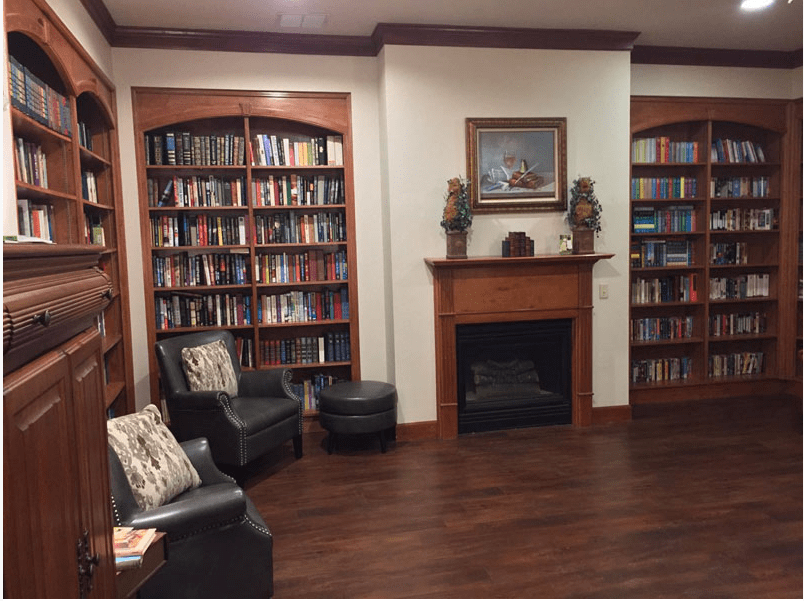 A cozy library room with wooden bookshelves, a fireplace, and comfortable seating.