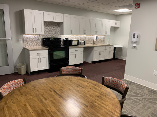 A modern kitchen area in an office, featuring a dining table and various appliances.