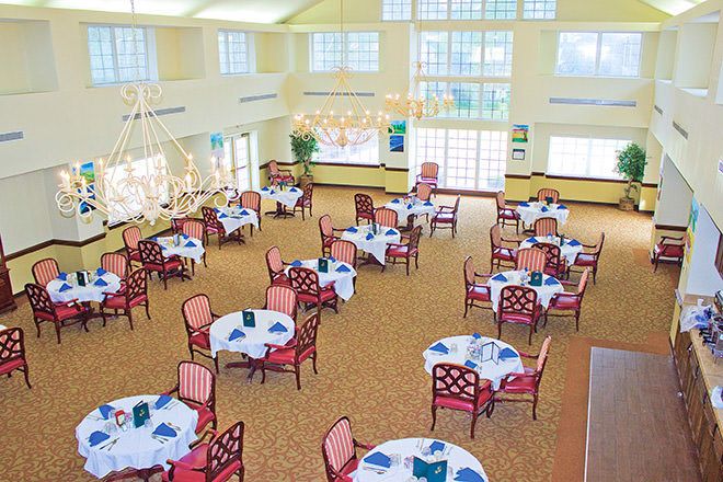An elegant dining room with well-arranged tables and chairs, featuring chandeliers and decorative table settings.