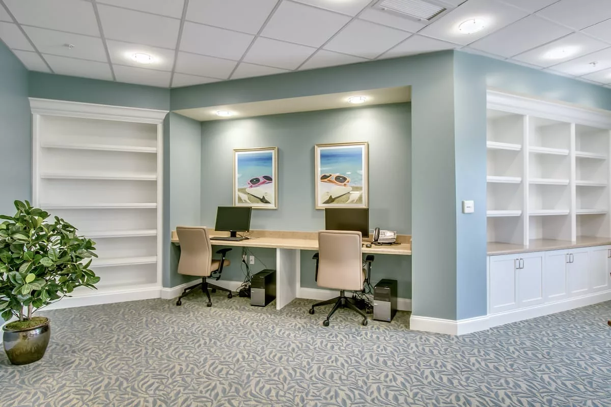 A modern office area with two workstations, equipped with computers and chairs, featuring built-in bookshelves and wall art.
