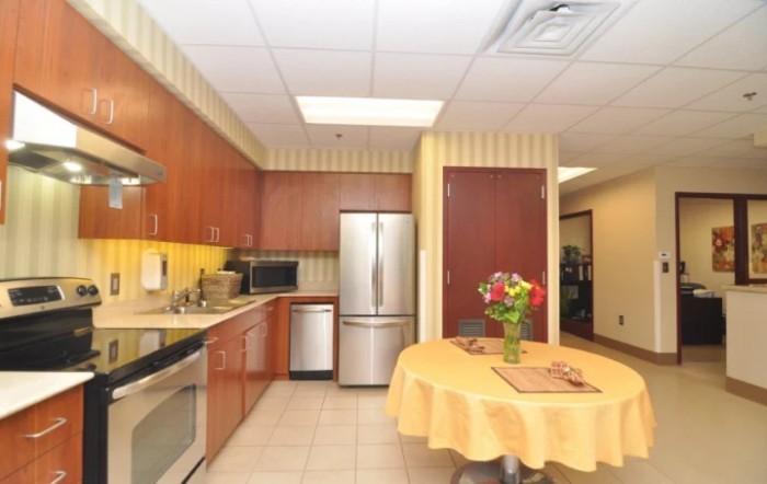 A modern kitchen with wood cabinets and stainless steel appliances, featuring a table adorned with a floral arrangement.