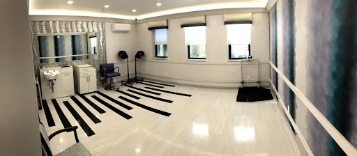 An empty dance studio featuring a polished wooden floor, large windows allowing natural light, and marked areas on the floor.