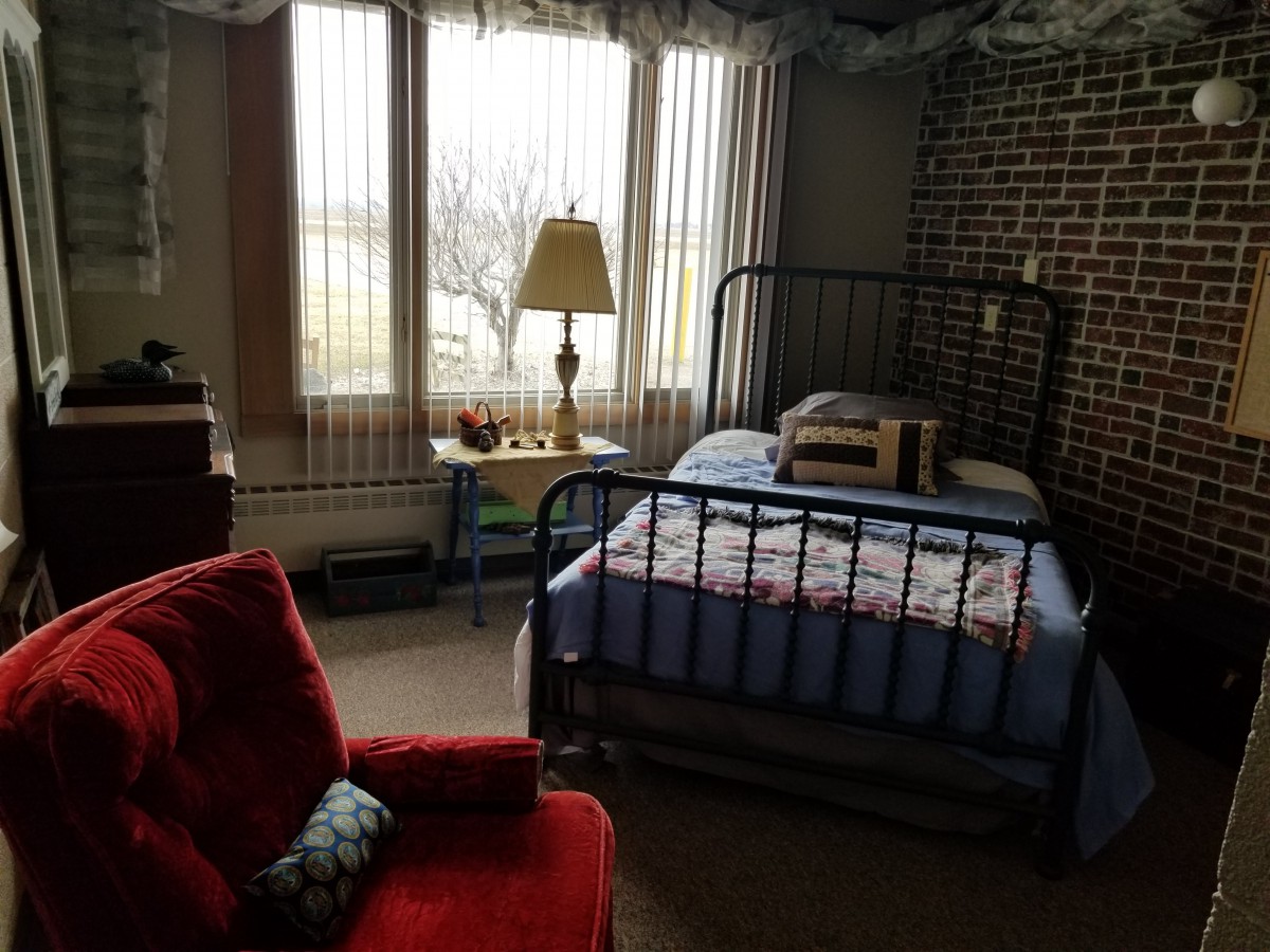 Cozy bedroom with a metal-framed bed, red chair, and a large window bringing in natural light.