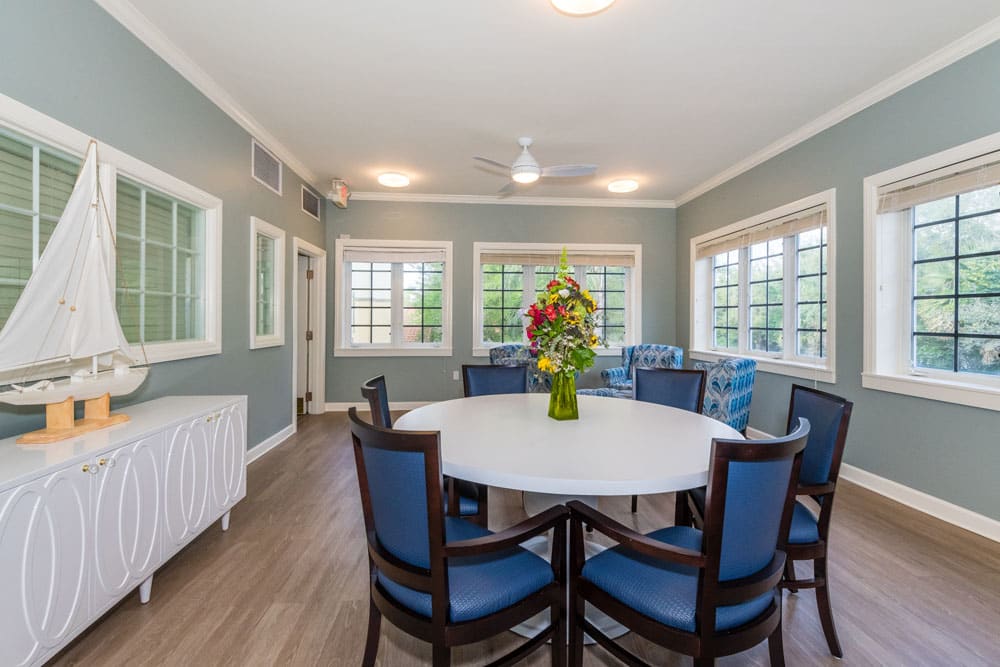 A bright dining room with a round table, surrounded by chairs, and a vibrant flower arrangement in the center.
