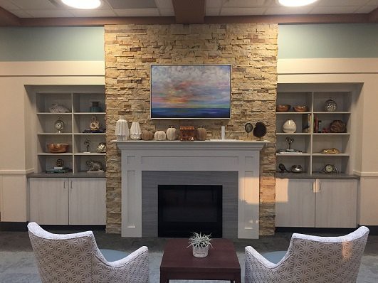 A cozy living room featuring a stone fireplace surrounded by built-in shelves filled with decorative items, and a seating area facing the fireplace.